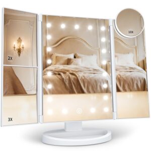 HUONUL trifold vanity mirror with built‑in LED lights around the central panel, mounted on a white base. The left panel shows 2X and 3X magnification sections, while a detachable circular 10X mirror is attached to the upper right corner. The mirror’s reflection displays a beige bedroom with an upholstered headboard, pillows, and wall sconce lighting, highlighting the mirror’s brightness and clarity