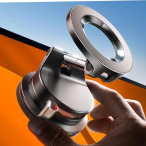 Close‑up of a sleek metallic MagSafe car mount being held by a hand, showing its circular magnetic ring and sturdy hinge design against a bright orange background and blue sky. The image highlights the mount’s premium build and precision engineering.