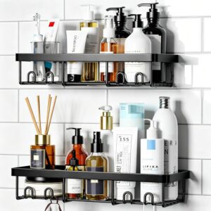 Two black metal Moforoco shower caddy shelves mounted on a white tiled bathroom wall. Each shelf holds an assortment of neatly arranged toiletries—shampoo, conditioner, lotion, and skincare bottles in black, white, and amber tones. The top shelf features pump bottles and tubes labeled “Shampoo” and “Herbivore,” while the bottom shelf includes a reed diffuser, amber bottles, and white containers. The overall look is clean, modern, and organized, showcasing the caddy’s sleek farmhouse‑style design and ample storage capacity.