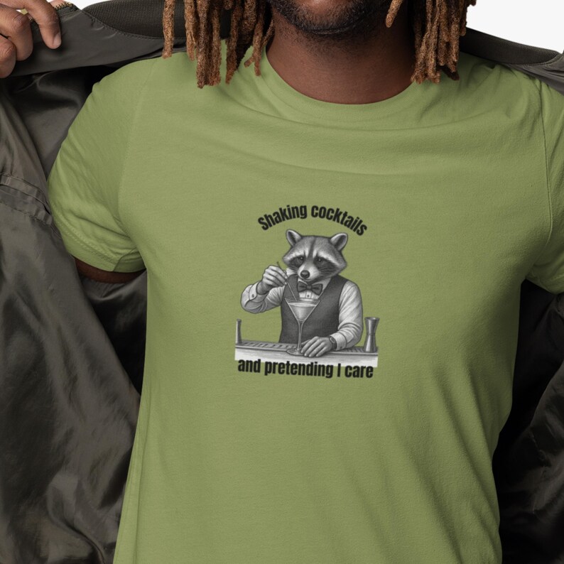 A light green shaking cocktails shirt featuring a raccoon dressed as a bartender stirring a drink with the text “Shaking cocktails and pretending I care,” styled casually with a jacket.