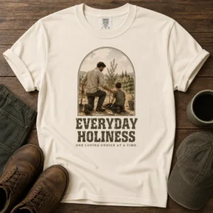 A cream everyday holiness shirt featuring a vintage illustration of a father and son planting a tree with the text “Everyday Holiness – One Loving Choice at a Time.”