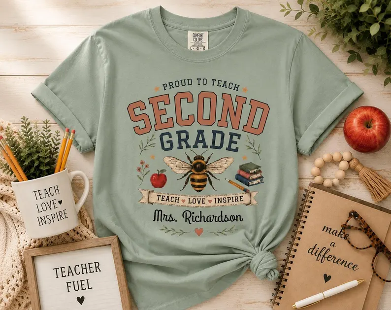 A sage green second grade teacher shirt featuring a vintage bee illustration, books, and apples with the text “Proud to Teach Second Grade – Teach • Love • Inspire,” styled with teacher accessories.