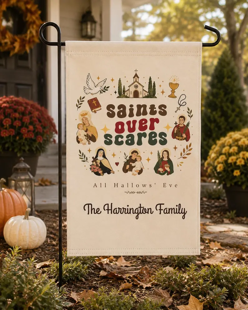 A cream saints over scares flag featuring vintage Catholic illustrations of saints, a church, and faith symbols with the text “Saints Over Scares – All Hallows’ Eve,” displayed outdoors with pumpkins and fall flowers.
